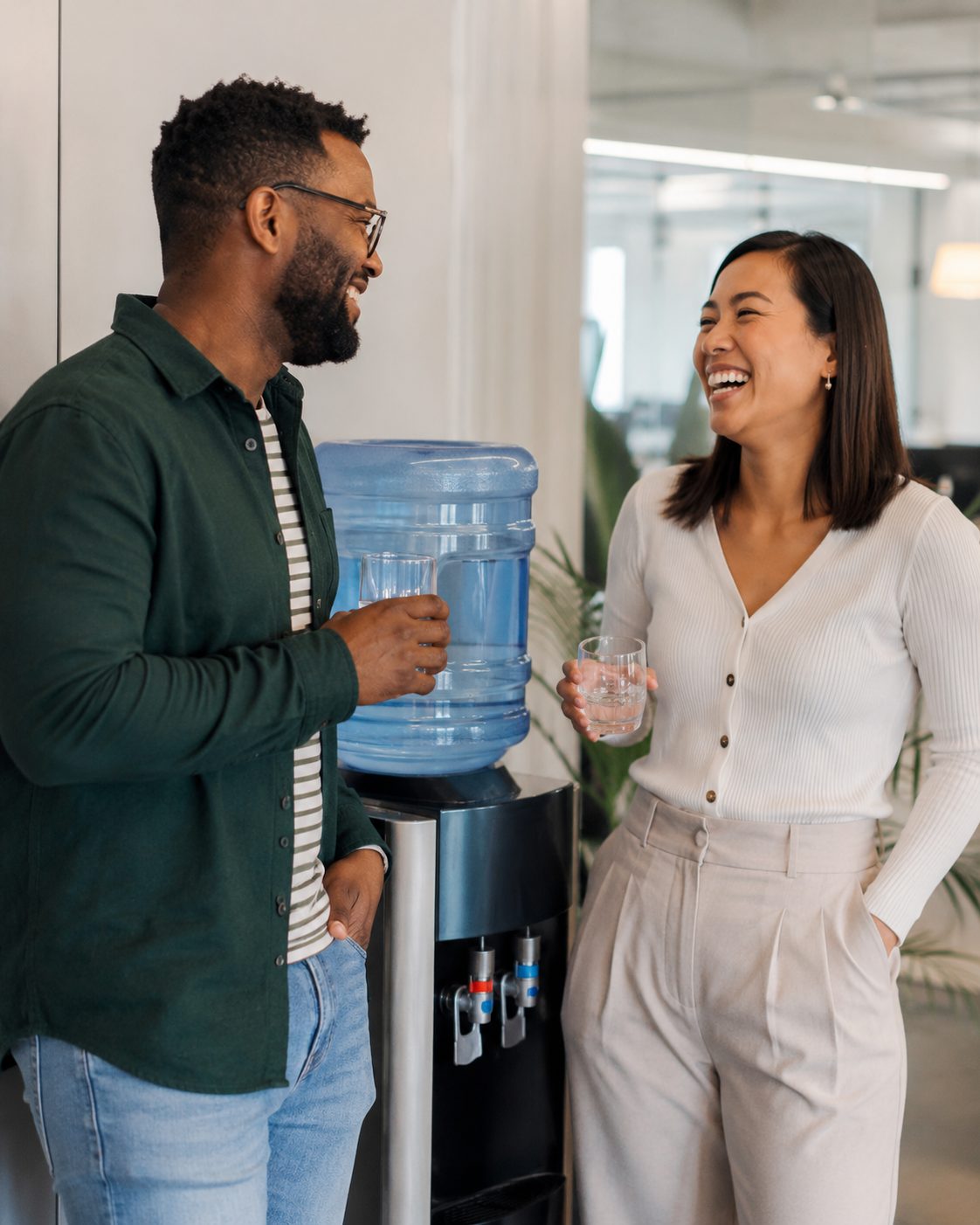 Two colleagues laughing by an office water cooler